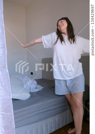 Woman in homewear stands by bed after waking starting a new day with mattress and pillow supporting healthy sleep and recovery at night Woman in homewear stands by bed after waking starting a new day with mattress and pillow supporting healthy sleep and recovery at night 138429697