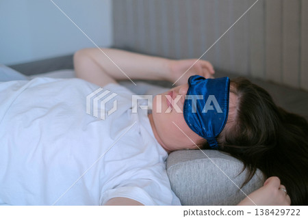 Woman in white pajamas rests with orthopedic pillow and sleep mask, deep restorative sleep and comfort for healthy rest 138429722