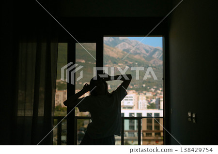 Woman in pajamas starts day stretching by window with mountain view fresh air relaxed mood and peaceful morning routine at home 138429754