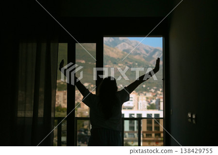 Woman in pajamas waking up in the morning stretching and opening window with mountain view calm routine cozy atmosphere natural light Woman in pajamas waking up in the morning stretching and opening window with mountain view calm routine cozy atmosphere natural light 138429755
