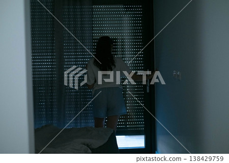 Morning in bedroom woman approaching panoramic window with electric blackout curtains showing smart home technology and customizable lighting atmosphere 138429759