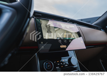 Close up interior shows a large touchscreen with 360 parking camera and rear guidelines, tan dashboard and red trim, soft light, shallow depth, workshop inspection focus. 138429767