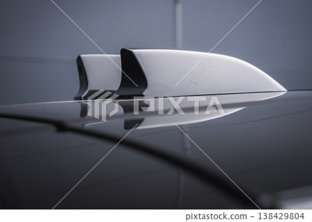 Close up of white shark fin roof antenna and smaller fin on glossy roof, mirrored on surface in an indoor workshop with cool lighting, emphasizing high end design. Close up of white shark fin roof antenna and smaller fin on glossy roof, mirrored on surface in an indoor workshop with cool lighting, emphasizing high end design. 138429804