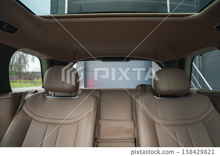Tan leather rear seats with sculpted headrests face the back window and sunroof. Soft lighting reveals stitching, chrome details, and a modern facility outside. Tan leather rear seats with sculpted headrests face the back window and sunroof. Soft lighting reveals stitching, chrome details, and a modern facility outside. 138429821