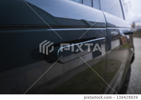 A shallow depth close view shows a flush door handle on a dark luxury SUV. Glossy bodywork reflects a service bay setting, suggesting dealership care and precision. A shallow depth close view shows a flush door handle on a dark luxury SUV. Glossy bodywork reflects a service bay setting, suggesting dealership care and precision. 138429839