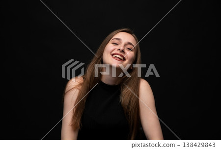 Happy young woman posing on a black background, expressing joy and laughter with a positive emotion and vibrant energy Happy young woman posing on a black background, expressing joy and laughter with a positive emotion and vibrant energy 138429843