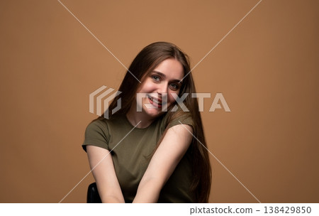Young brunette woman with long hair smiling broadly while sitting in a studio, looking at camera with happy expression 138429850