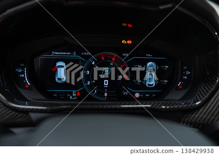 Close up digital cluster shows central tachometer and Park, 3D car diagrams, temperatures, and warnings, carbon fiber trim, luxury Lamborghini Urus SE interior in a workshop setting. Close up digital cluster shows central tachometer and Park, 3D car diagrams, temperatures, and warnings, carbon fiber trim, luxury Lamborghini Urus SE interior in a workshop setting. 138429938