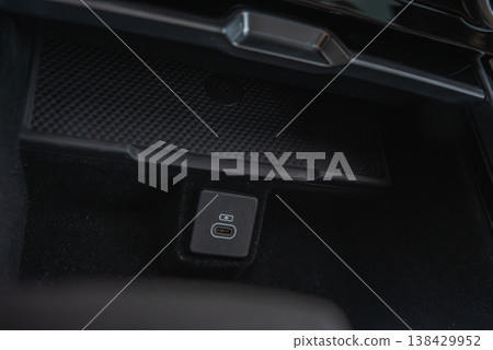 A close up interior shows a center console storage with rubber tray and dual USB C port in black carpeting, minimalist finish, subtle lighting, indoors at a workshop 138429952