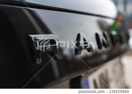 Close view of Range Rover rear letters in focus, glossy black paint reflects light. Soft blur hides other letters in a well lit workshop with luxury models nearby. 138429969