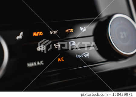 Illuminated AUTO, SYNC, A C, MAX defrost, and rear defog icons glow on a glossy panel with a rotary dial near 21 C, shot indoors in a high end workshop with shallow depth of field Illuminated AUTO, SYNC, A C, MAX defrost, and rear defog icons glow on a glossy panel with a rotary dial near 21 C, shot indoors in a high end workshop with shallow depth of field 138429971