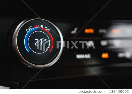 A close up shows a climate control dial at 21.5 C with blue and red arcs, seat and fan icons marked Push and Pull, and orange backlit AUTO and recirculation buttons in low light. A close up shows a climate control dial at 21.5 C with blue and red arcs, seat and fan icons marked Push and Pull, and orange backlit AUTO and recirculation buttons in low light. 138430005