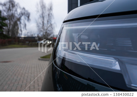 Close up shows right headlight and front fender of a luxury Range Rover SUV, sharp LED elements and glossy dark paint in overcast light, blurred forecourt and leafless trees suggest late afternoon. Close up shows right headlight and front fender of a luxury Range Rover SUV, sharp LED elements and glossy dark paint in overcast light, blurred forecourt and leafless trees suggest late afternoon. 138430022