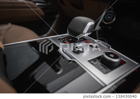 Close up of a luxury SUV center console shows electronic gear selector, metallic rotary drive mode knobs, glossy black trim, and small display under soft diffused lighting. Close up of a luxury SUV center console shows electronic gear selector, metallic rotary drive mode knobs, glossy black trim, and small display under soft diffused lighting. 138430040