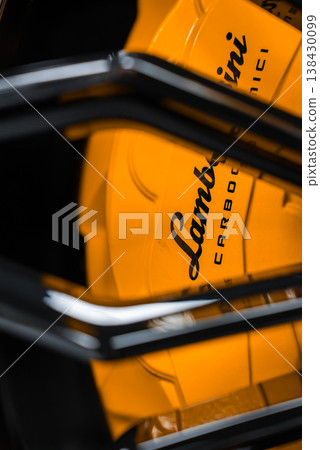Tight angled close up shows a yellow Lamborghini brake caliper and logo through glossy black spokes, indoors with controlled lighting, shallow depth, and strong contrast. 138430099