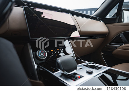 Close up interior shows central console and dashboard of a luxury SUV, with floating infotainment screen, dual climate dials at 21 C, and glossy tunnel gear selector 138430108