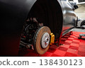 Close up of a luxury SUV on jack stands with front wheel off, showing drilled rotor and gold caliper on a red checkered floor in a professional service bay, low angle. 138430123