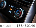 Close up focuses on a climate control dial set to 21C, blue to red ring, soft touch black trim, metallic bezel, and icons, shallow depth of field, glossy reflections. 138430140