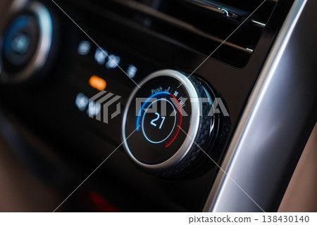 Close up focuses on a climate control dial set to 21C, blue to red ring, soft touch black trim, metallic bezel, and icons, shallow depth of field, glossy reflections. 138430140