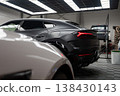 A matte black Lamborghini Urus stands in a lit workshop, sharp taillights visible. A Mercedes AMG and a new Range Rover are serviced, one on a lift, tools around. 138430143