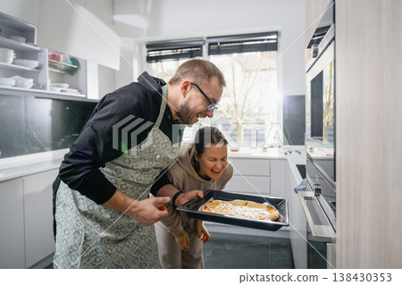 Happy couple laughing at freshly baked pizza in kitchen Happy couple laughing at freshly baked pizza in kitchen 138430353