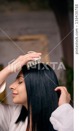 Woman massaging scalp with brush during hair care routine Woman massaging scalp with brush during hair care routine 138430788