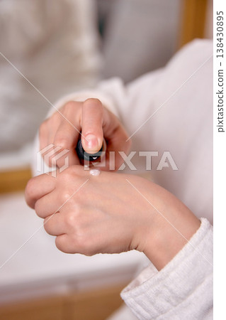 Woman applying skincare cream on hand during beauty routine. 138430895