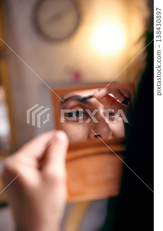 Woman grooming eyebrow looking in mirror during beauty routine. 138430897