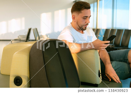 Traveler with backpack in airport lounge using built in charging in seat staying connected working and preparing for journey with modern technology and mobility Traveler with backpack in airport lounge using built in charging in seat staying connected working and preparing for journey with modern technology and mobility 138430923