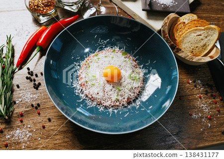 Gourmet beef tartare topped with a fresh egg yolk and grated Parmesan cheese. Served with toasted bread slices, red chili peppers, and rosemary. Perfect for a sophisticated dining experience Gourmet beef tartare topped with a fresh egg yolk and grated Parmesan cheese. Served with toasted bread slices, red chili peppers, and rosemary. Perfect for a sophisticated dining experience 138431177