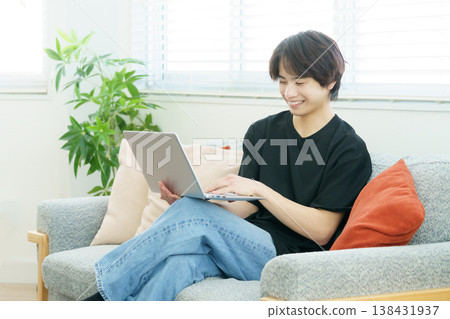 A young Japanese man is sitting on a sofa and operating his laptop. A young Japanese man is sitting on a sofa and operating his laptop. 138431937