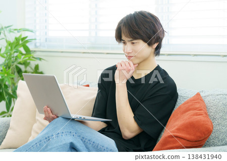 A young Japanese man is sitting on a sofa and operating his laptop. A young Japanese man is sitting on a sofa and operating his laptop. 138431940