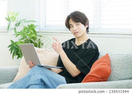 A young Japanese man is sitting on a sofa and operating his laptop. A young Japanese man is sitting on a sofa and operating his laptop. 138431944