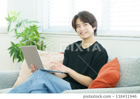 A young Japanese man is sitting on a sofa and operating his laptop. A young Japanese man is sitting on a sofa and operating his laptop. 138431946