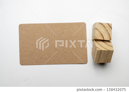 Top-down view of a blank brown kraft paper card and two wooden blocks on a white surface. Ideal for minimalist branding mockups and creative design Top-down view of a blank brown kraft paper card and two wooden blocks on a white surface. Ideal for minimalist branding mockups and creative design 138432075