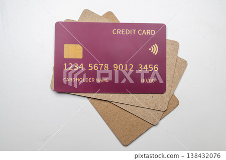 A top-down view of a pink credit card with a chip and contactless symbol lying on a stack of recycled cardboard cards, representing sustainable banking and finance 138432076