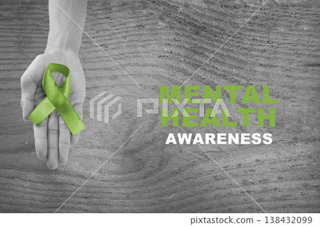 Grayscale image of a hand holding a green ribbon with Mental Health Awareness text on a rustic wooden background. A powerful symbol of support for psychological well-being 138432099