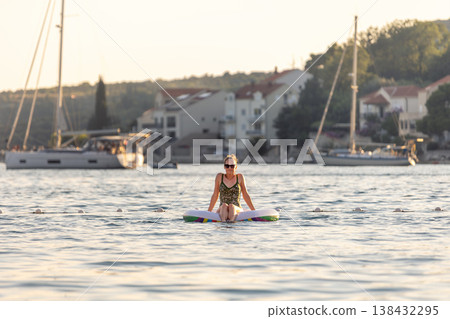 Scenic view woman relax alone inflatable raft calm sea coastal village marina sailboats warm sunset light. Peaceful summer atmosphere solo vacation lifestyle freedom relaxation mediterranean scenery Scenic view woman relax alone inflatable raft calm sea coastal village marina sailboats warm sunset light. Peaceful summer atmosphere solo vacation lifestyle freedom relaxation mediterranean scenery 138432295