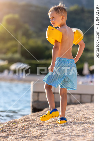 Little smile boy wear swimwear inflatable arm walk clear sea water pebble beach sunny warm sunset summer vacation. Carefree childhood warm sunlight bay coast landscape relax family holiday Little smile boy wear swimwear inflatable arm walk clear sea water pebble beach sunny warm sunset summer vacation. Carefree childhood warm sunlight bay coast landscape relax family holiday 138432297