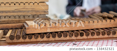 Wooden cigar molds filled rolled tobacco cigars display table during traditional handmade production process. Artisan workshop scene classic tool shape pressing cigars historic tobacco craft industry Wooden cigar molds filled rolled tobacco cigars display table during traditional handmade production process. Artisan workshop scene classic tool shape pressing cigars historic tobacco craft industry 138432321