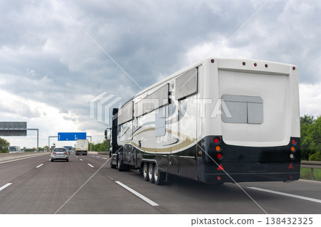 Large recreational vehicle camper trailer driving on highway under dramatic overcast cloudy sky during travel journey. Mobile motorhome transport used for vacation road trip tourism Large recreational vehicle camper trailer driving on highway under dramatic overcast cloudy sky during travel journey. Mobile motorhome transport used for vacation road trip tourism 138432325