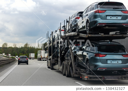 Tow truck car carrier semi trailer on highway carrying batch of new wrapped electric SUVs on motorway road at sunset evening time. Business distribution logistics service. Lorry driving highway Tow truck car carrier semi trailer on highway carrying batch of new wrapped electric SUVs on motorway road at sunset evening time. Business distribution logistics service. Lorry driving highway 138432327