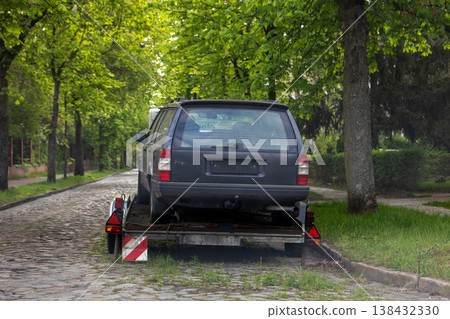 Old station wagon car loaded transport trailer parked on quiet cobblestone german city street urban park area for free of charge parking. Vehicle ready towing or relocation. roadside transport scene Old station wagon car loaded transport trailer parked on quiet cobblestone german city street urban park area for free of charge parking. Vehicle ready towing or relocation. roadside transport scene 138432330