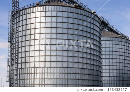 Scenic view of big modern steel agricultural grain granary silos cereal bin storage warehouse against blue sky. Agribusiness farmland rural industry silo landscape scene. Mill store farm facility 138432357