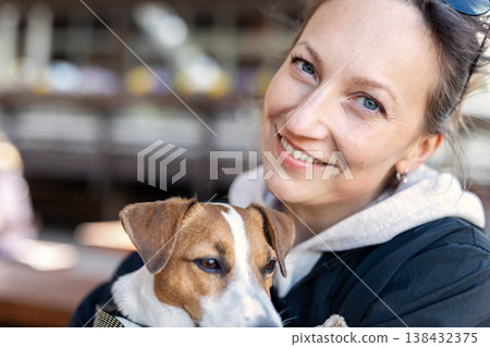 Smiling woman blue eyes hugs small jack russel terrier dog warm sunlight candid portrait affection companionship. Friendly moment shows trust happiness gentle bond between person and loyal pet Smiling woman blue eyes hugs small jack russel terrier dog warm sunlight candid portrait affection companionship. Friendly moment shows trust happiness gentle bond between person and loyal pet 138432375