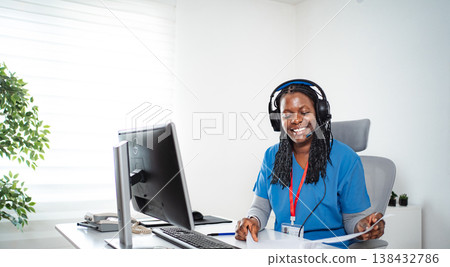 Healthcare professional working on computer, wearing headset Healthcare professional working on computer, wearing headset 138432786