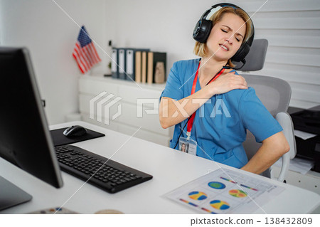 Healthcare worker experiencing shoulder pain at an office desk Healthcare worker experiencing shoulder pain at an office desk 138432809
