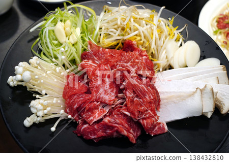 Fresh raw beef bulgogi with assorted vegetables including green onions, bean sprouts, and enoki mushrooms on a black plate, traditional Korean marinated beef preparation before cooking Fresh raw beef bulgogi with assorted vegetables including green onions, bean sprouts, and enoki mushrooms on a black plate, traditional Korean marinated beef preparation before cooking 138432810