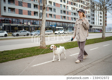 Young woman walking dog on city street sidewalk 138432872
