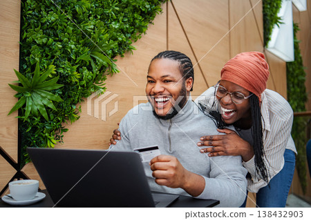Happy young adult couple enjoying online shopping with credit card Happy young adult couple enjoying online shopping with credit card 138432903
